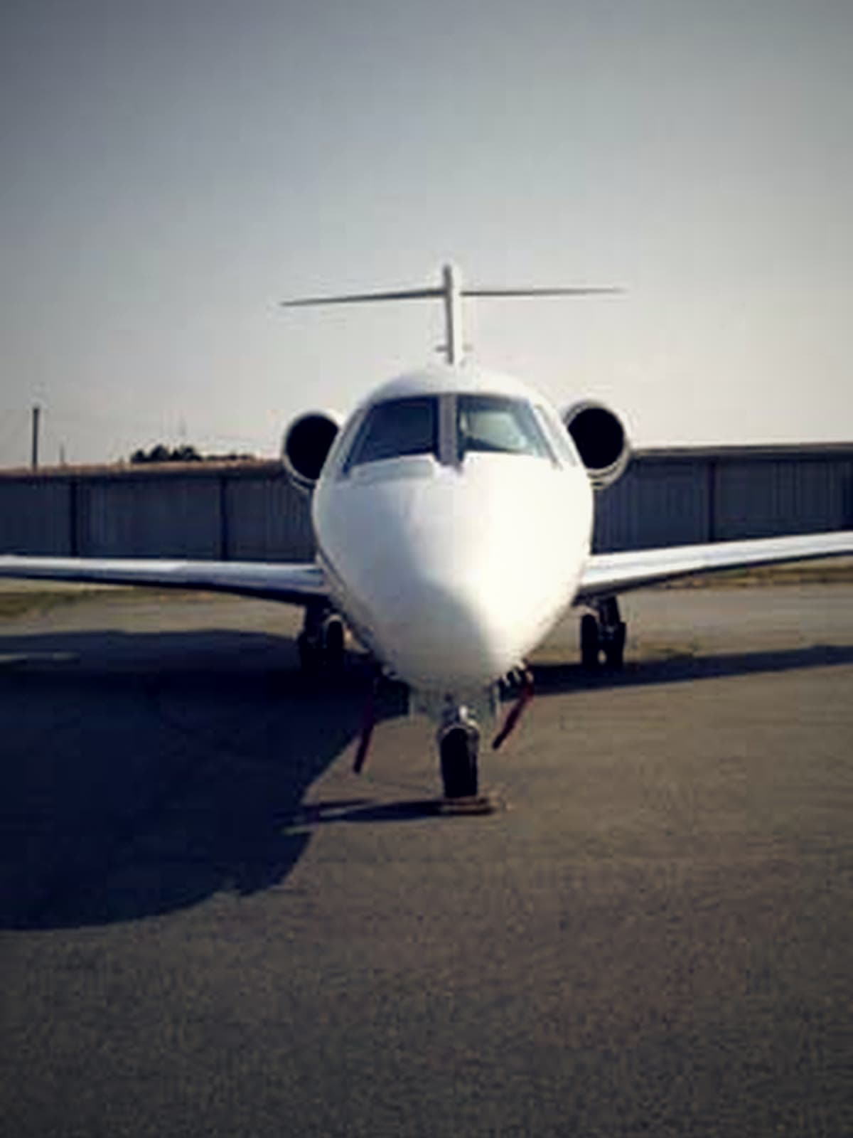 A business jet on the KTOC ramp with T-hangars behind it.